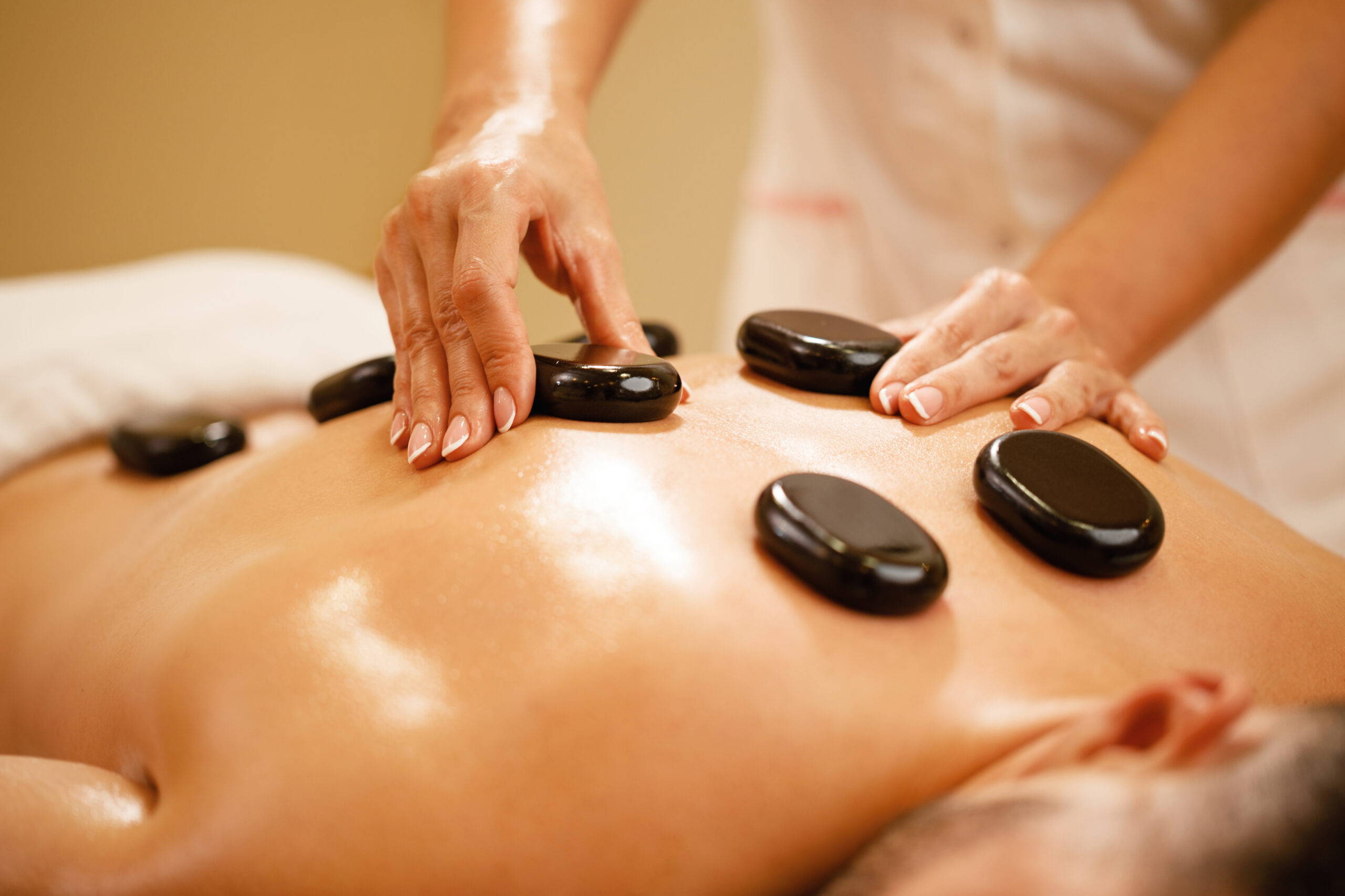 Close-up of therapists placing hot stones on man's back during lastone therapy at the spa.